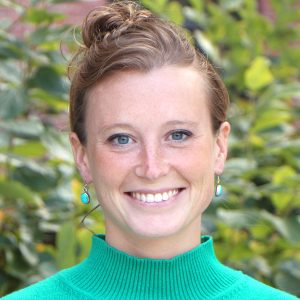 Headshot of Camille Testard smiling wearing a teal sweater, with green leaves in the background