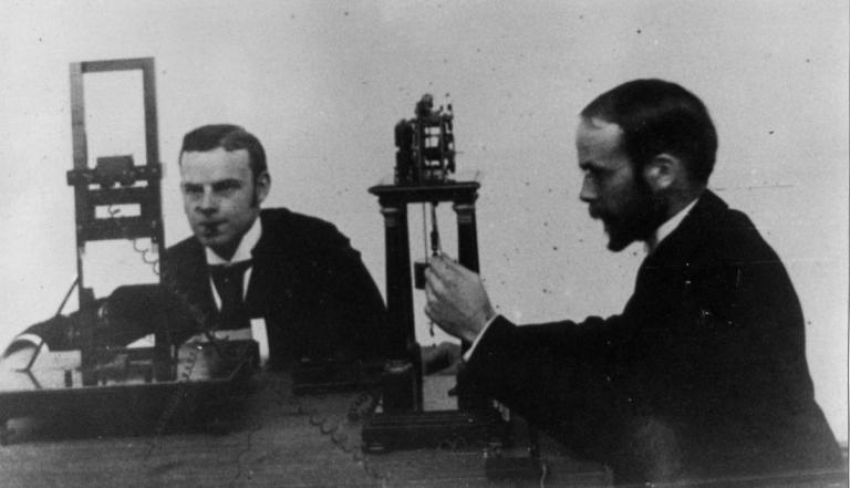 A black and white image of Cattell and his subject, using the Hipp Chronoscope and a Cattell Gravity Chronometer for a reaction-time experiment.