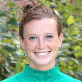 Headshot of Camille Testard smiling wearing a teal sweater, with green leaves in the background