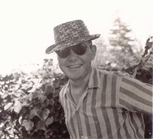 A black and white photo of Bush smiling outside, wearing sunglasses and a hat.